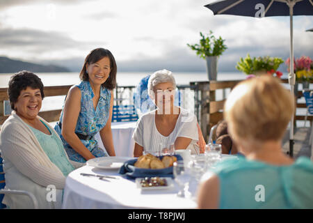 Zwei reife weibliche Freunde in ein Restaurant am Meer Lächeln zu Mittagessen und ein Lachen mit einigen Bekannten, die gekommen sind, um Hallo zu sagen. Stockfoto