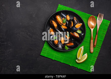 Meeresfrüchte Muscheln und Basilikumblätter in einer schwarzen Platte auf Bambus matte und Tisch aus Stein. Ansicht von oben. Stockfoto