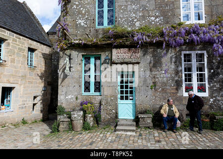 Zwei ältere Touristen sitzen im traditionellen Haus aus Stein mit Glyzinien wächst an Fassaden in erhaltenen mittelalterlichen Dorf von Locronan in der Bretagne, Frankreich Stockfoto