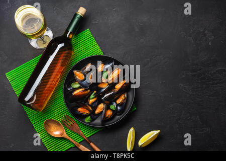 Meeresfrüchte, Muscheln, Basilikumblätter in eine schwarze Platte mit Wein Bootle, Weinglas, Zitrone, hölzernen Löffel und Gabel auf grüner Bambus matte und Tisch aus Stein. Ansicht von oben Stockfoto