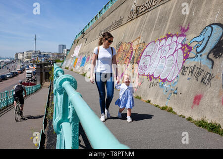 Brighton, UK. 14 Mai, 2019. Eine junge Mutter und ihre Tochter 2 Jahre genießen Sie einen Spaziergang entlang der Küste von Brighton an einem heißen sonnigen Tag mit schönem Wetter Prognose für die nächsten Tage in ganz Großbritannien. Foto: Simon Dack/Alamy leben Nachrichten Stockfoto