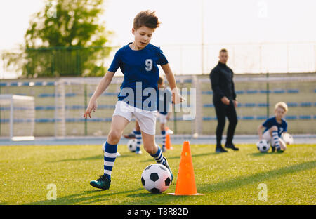 Jungen Training Fußball Dribbling in einem Feld. Kinder die Kugel. Spieler entwickeln Fußball Dribblings. Kinder Training mit Kugeln und Kegel. S Stockfoto