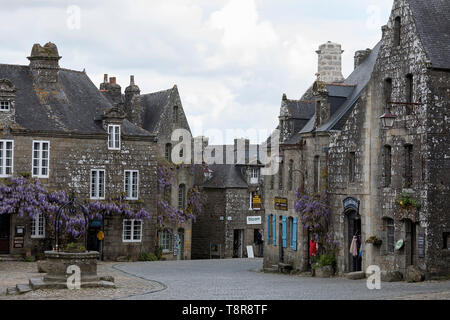 Traditionelle Häuser aus Stein mit Glyzinien wachsen auf Fassaden mit blauen Fensterläden und Türen in erhaltenen mittelalterlichen Dorf von Locronan in der Bretagne, Frankreich Stockfoto