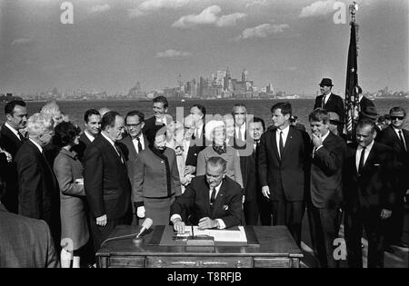 Präsident Lyndon B. Johnson unterzeichnet das Zuwanderungsgesetz als Vizepräsident Hubert Humphrey, Lady Bird Johnson, Muriel Humphrey, Senator Edward (Ted) Kennedy, Senator Robert F. Kennedy, und die anderen schauen zu. Liberty Island, New York City, New York, 3. Oktober, 1965 Stockfoto