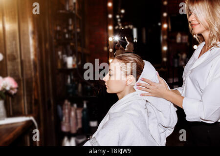 Die attraktive Friseur gewaschen Kopf des blonden Mädchen und Trocknen, mit weißen Handtuch im Schönheitssalon. Frau entspannend nach dem Waschen und Hai behandeln Stockfoto