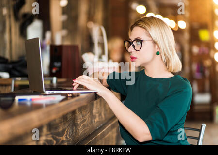 Indoor Nahaufnahme Portrait von attraktiven Blondine konzentriert Freelancer, Administrator, Manager in große Gläser mit Laptop Computer. Selektive konzentrieren. B Stockfoto