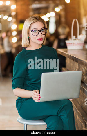 Portrait of Beauty Salon empfangsdame am Arbeitsplatz. Ernsthafte charmante Business Frau im grünen Pullover sitzen auf Stuhl mit den Händen auf die Tastatur, Schreiben, Stockfoto