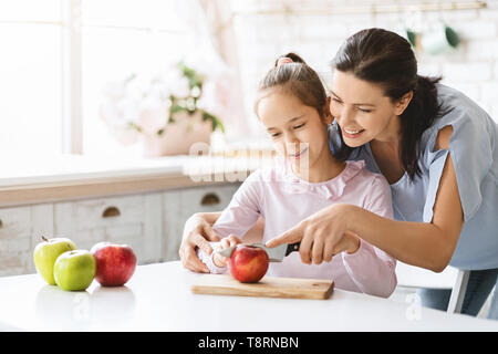 Mom Lehre süße Mädchen zu schneiden Apple mit Messer Stockfoto