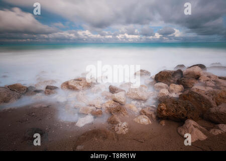 Eingehende Flut auf einem felsigen Strand unter stürmischen Himmel, Langzeitbelichtung Bild Stockfoto