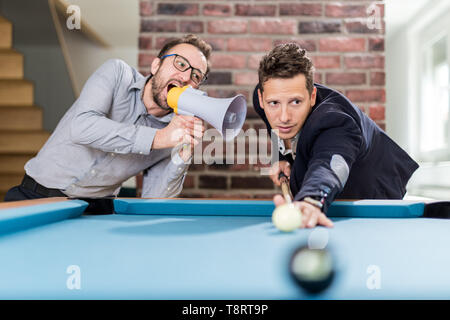 Billard Spieler, die darauf abzielt, die Kugel, während sein Freund ihn störenden mit Megaphon. Stockfoto