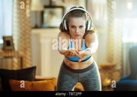 Junge Frau in Kopfhörer im Sport Kleidung an moderne Home ausdehnen. Stockfoto