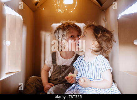 Zwei glückliche Kind Kinder spielen drinnen in der Pappe Haus zu Hause, küssen. Stockfoto