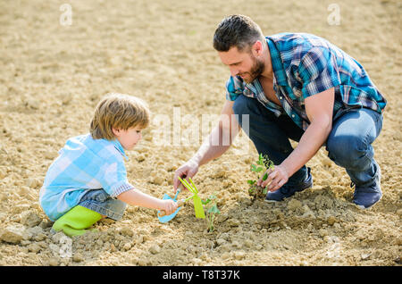 Kleiner Junge Kind helfen Vater in der Landwirtschaft. reichen natürlichen Boden. Eco Farm. Vater und Sohn Blumen Pflanzen im Boden. neues Leben. Böden, Düngemitteln. happy Earth Day. Stammbaum. Tag der Erde. Das Sitzen auf dem Boden. Stockfoto