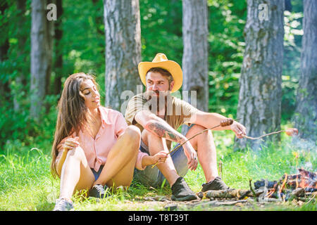 Paar vorbereiten gebratene Würstchen snack Natur Hintergrund. Wanderung Picknick traditionelle geröstet Essen. Hipster und Mädchen braten Würstchen. Verliebtes Paar camping Wald braten Würstchen. Camping und Picknick. Stockfoto