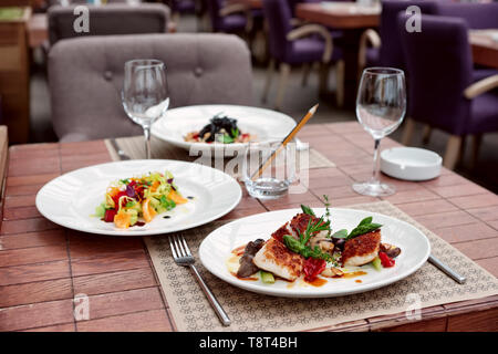 Fischfilet mit Gemüse und anderen Lebensmitteln auf Tisch im Restaurant Stockfoto
