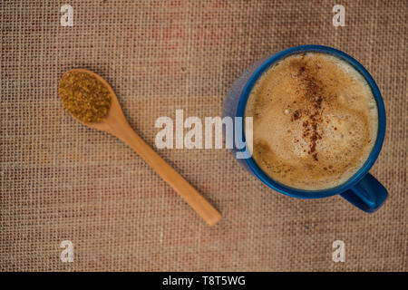 Blaue Tasse Kaffee mit Milch und Zimt mit hölzernen Löffel gefüllt mit Rohrzucker Stockfoto