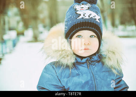 Baby im Winter Overalls in ein Tuch eingewickelt Spaziergänge auf eine verschneite Straße und formt aus Schnee. Stockfoto