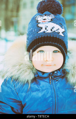 Baby im Winter Overalls in ein Tuch eingewickelt Spaziergänge auf eine verschneite Straße und formt aus Schnee. Stockfoto