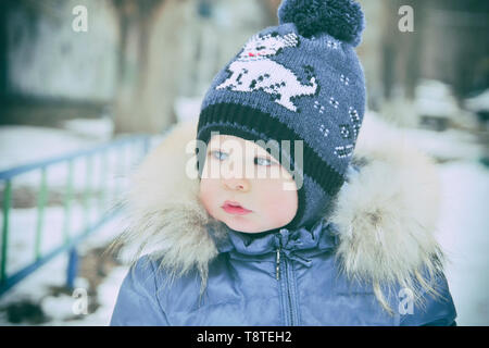 Baby im Winter Overalls in ein Tuch eingewickelt Spaziergänge auf eine verschneite Straße und formt aus Schnee. Stockfoto