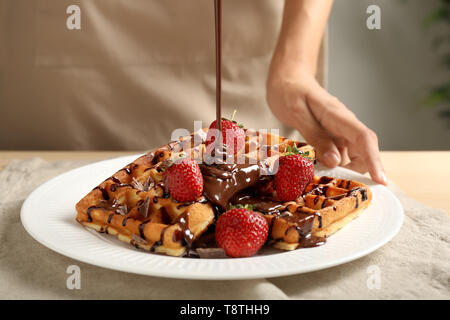 Frau gießen Schokolade Soße auf leckere selbstgemachte Waffeln, Nahaufnahme Stockfoto