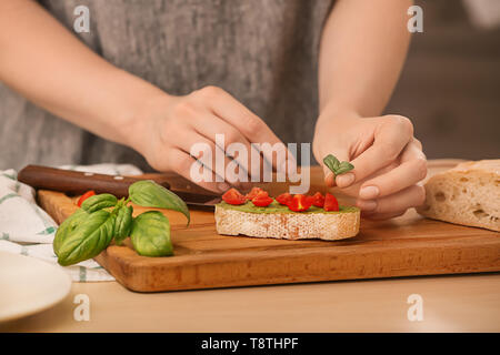 Frau Vorbereitung sandwich Sauce mit Basilikum und Tomaten am Tisch Stockfoto