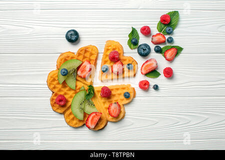 Herzförmige Waffeln Beeren und Kiwi Slices auf weißem Holz- Hintergrund Stockfoto