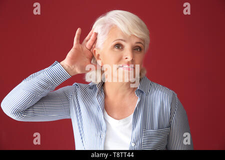 Porträt der reifen Frau, die versuchen, etwas auf Farbe Hintergrund zu hören Stockfoto