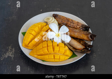 Im thailändischen Stil Dessert, gelbe Mango mit Banane klebriger Reis in Palmblättern. Gelbe Mango und klebriger Reis ist beliebt traditionelle Speisen von Thailand. Schließen u Stockfoto