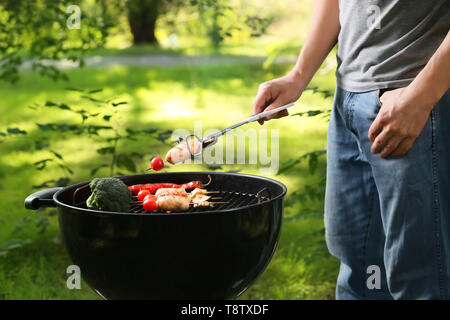 Mann kochen Würstchen und Gemüse am Grill im Freien Stockfoto