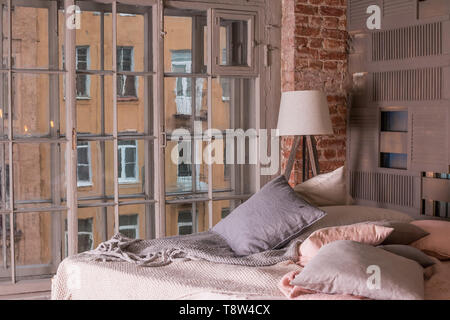 Loft Apartment Interieur. Minimalistische Einrichtung mit einfachen Bett aus Holz, Lampe, weiße Bettwäsche. Pastellfarben, großes Fenster. Gemütliche Zimmer Stockfoto