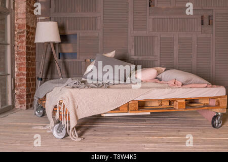 Loft Apartment Interieur. Minimalistische Einrichtung mit einfachen Bett aus Holz, Lampe, großes Fenster. Stilvolle Schlafzimmer im Loft Stil in Pastelltönen gestaltet. Platz kopieren Stockfoto