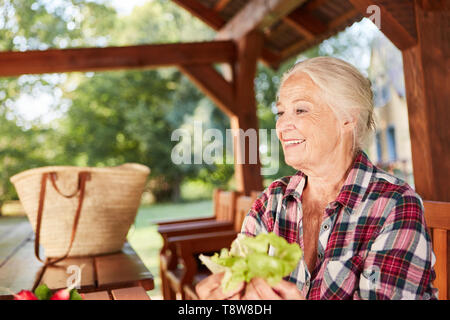 Lächelnde ältere Frau mit frischem Salat auf der Veranda auf dem Bauernhof Stockfoto