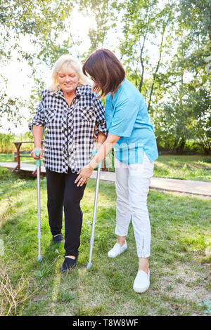 Stillende Frau Hilfen ältere Frau mit Krücken beim Laufen lernen in rehab Stockfoto