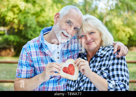 Amorous senior Paar hält ein Herz in den Händen und Umarmungen einander liebevoll Stockfoto