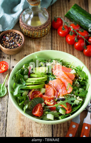 Diätmenü, veganes Essen. Gesunde Salate mit Quinoa, Rucola, Tomaten, Lachs und Avocado auf rustikalen Tisch. Freier Platz für Ihren Text. Stockfoto