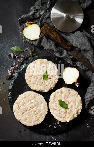 Rohe frische Schnitzel Burger aus Rindfleisch für hausgemachte Burger Kochen mit Gewürzen auf dem Schwarzen Brett. Ansicht von oben. Stockfoto