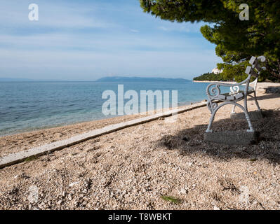 Holzbank am leeren Strand in der Nähe des Meeres in Tucepi, Kroatien Stockfoto