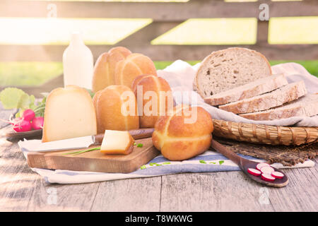 Traditionelle organische geräucherter Käse mit frischem Gemüse, Milch und Brot im Hintergrund an einem sonnigen Tag draußen auf Bio-bauernhof. Stockfoto