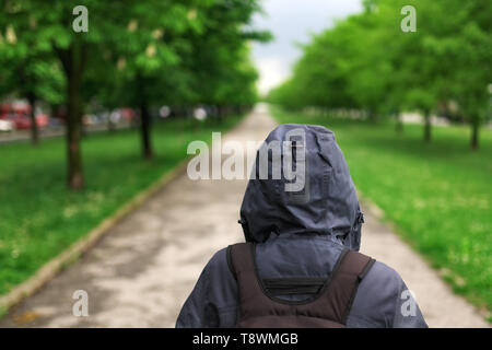 Ansicht der Rückseite des einsamen Hooded weibliche Person zu Fuß die Leere, mit Bäumen gesäumten Gasse Stockfoto