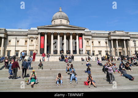 Touristen sitzen auf der Treppe vor der National Gallery am Trafalgar Square, London, UK
