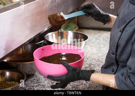 Thema kochen Schokolade. Nahaufnahme einer Hand. Junge kaukasier Frau Kochen mit Tattoo und in Uniform bereitet heiße Dicke Schokolade in einem Topf zu machen. Vergangenheit Stockfoto