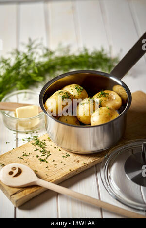Junge Kartoffeln im Topf mit Dill und Butter auf Holzbrett gekocht Stockfoto