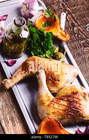 Gegrillte Hähnchenkeulen mit gerösteten Kürbis serviert, Pesto und frische Petersilie auf rustikalen Holztisch, Fleisch und Gemüse braten Abendessen Stockfoto