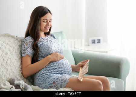 Schöne schwangere Frau mit Einrichtung in Form des Wortes Babys zu Hause Stockfoto