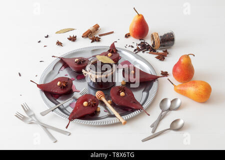 Hibiscus pochierte Birnen, süße Frucht Dessert. Silber Tablett mit Birnen, mit Haselnüssen, Lorbeerblätter verschönert, getrocknet Hibiskusblüten, Anis Sterne, und Stockfoto