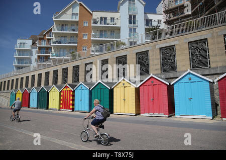 Menschen machen sich auf den Weg hinter Strand Hütten auf Boscombe Strand, als Sie das warme Wetter genießen. Stockfoto