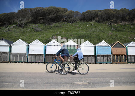 Menschen machen sich auf den Weg hinter Strand Hütten auf Boscombe Strand, als Sie das warme Wetter genießen. Stockfoto