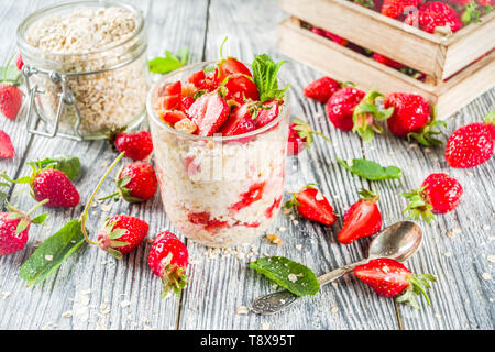 Sommer Ernährung gesundes Frühstück. Über Nacht Haferflocken in einem Glas, mit Stücken von Erdbeeren und Minze, mit frischen Beeren auf einem hölzernen Hintergrund, Stockfoto