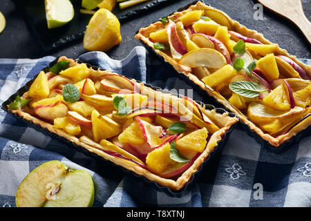 Französisch Ananas und Apfel süße öffnen Torten in rechteckigen tart Pfannen auf einer konkreten Tabelle mit Küchentuch, horizontale Ansicht von oben Stockfoto