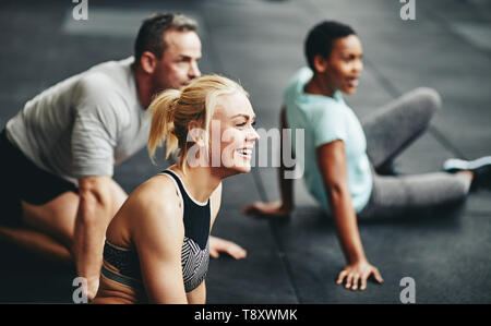 Vielfältige Gruppe von lächelnden Menschen in Sportkleidung sitzen zusammen auf einen Fitnessraum, eine Pause von Ihren Workout Stockfoto
